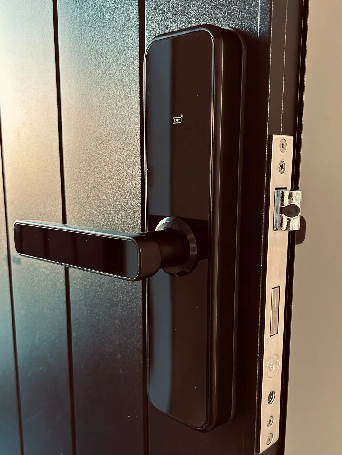 A black smart lever lock, keypad unlit, fitted to a grooved metal faced door