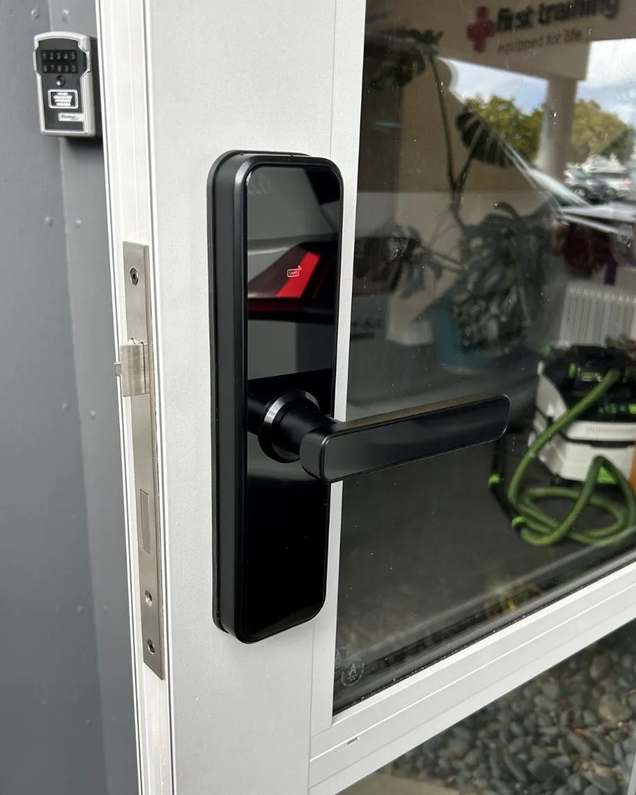 Black smart lock on a white aluminium commercial glazed door, with a key safe alongside
